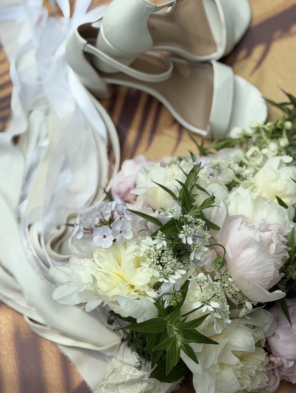 Bridal shoes beside a soft white and blush bouquet