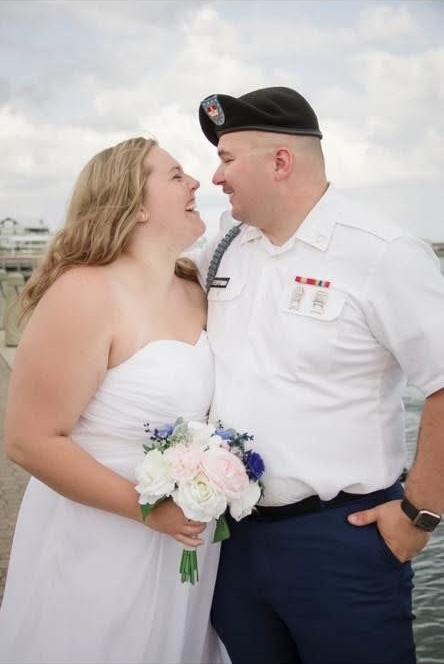 Bride and groom in uniform smiling at each other by the water